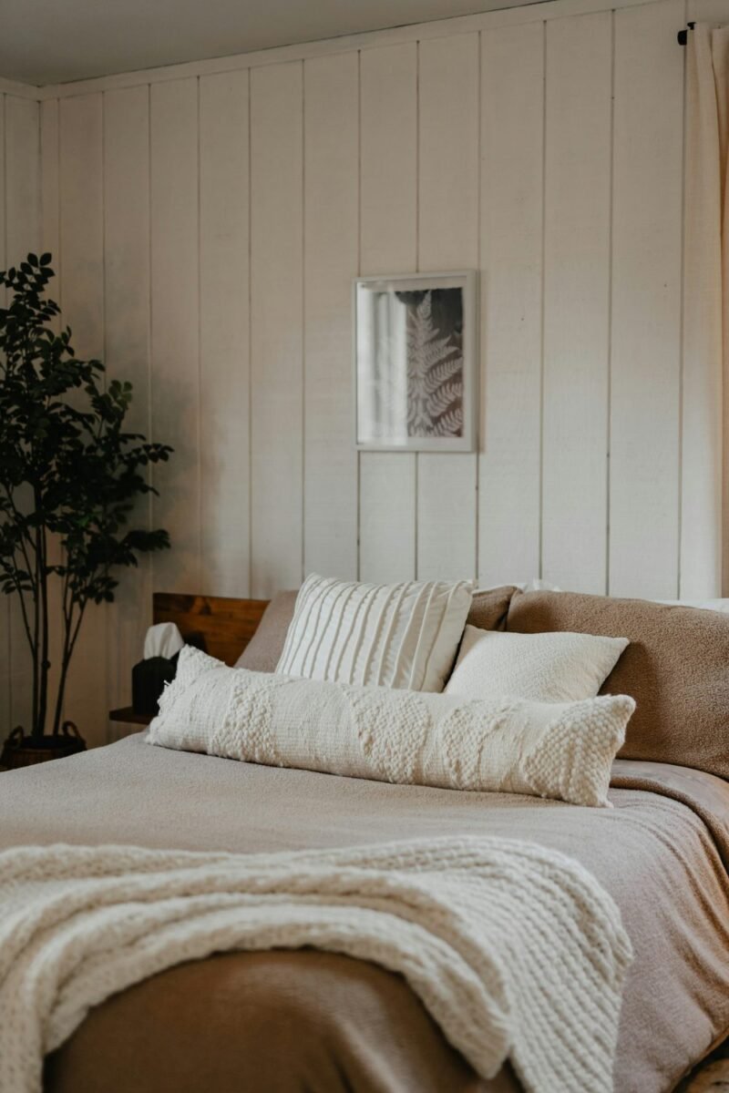 Bed layered with a chunky knit throw and mixed-texture cushions in a small bedroom