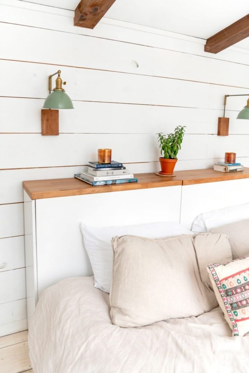 A floating shelf above the bed holding stacked books and a small plant