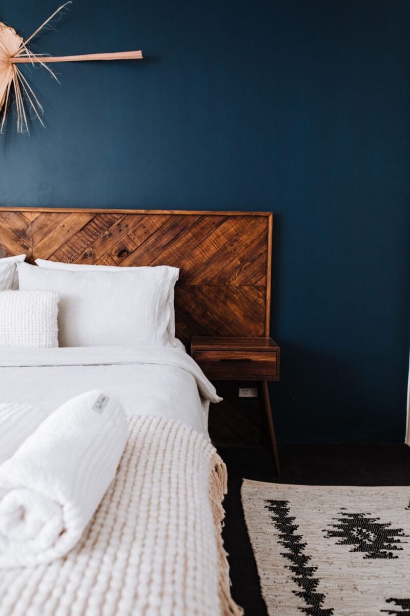 Moody small bedroom with a deep blue wall, a wooden headboard and soft white layered bedding
