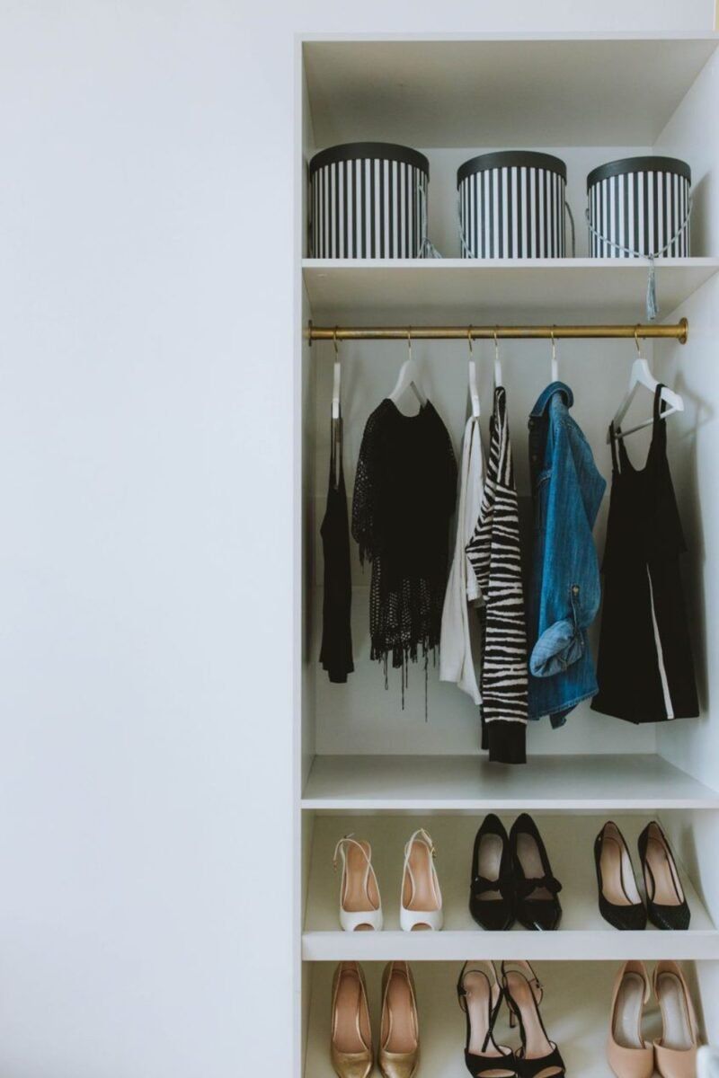 An organized closet with clothes on a rail, shoes below, and striped storage boxes up top