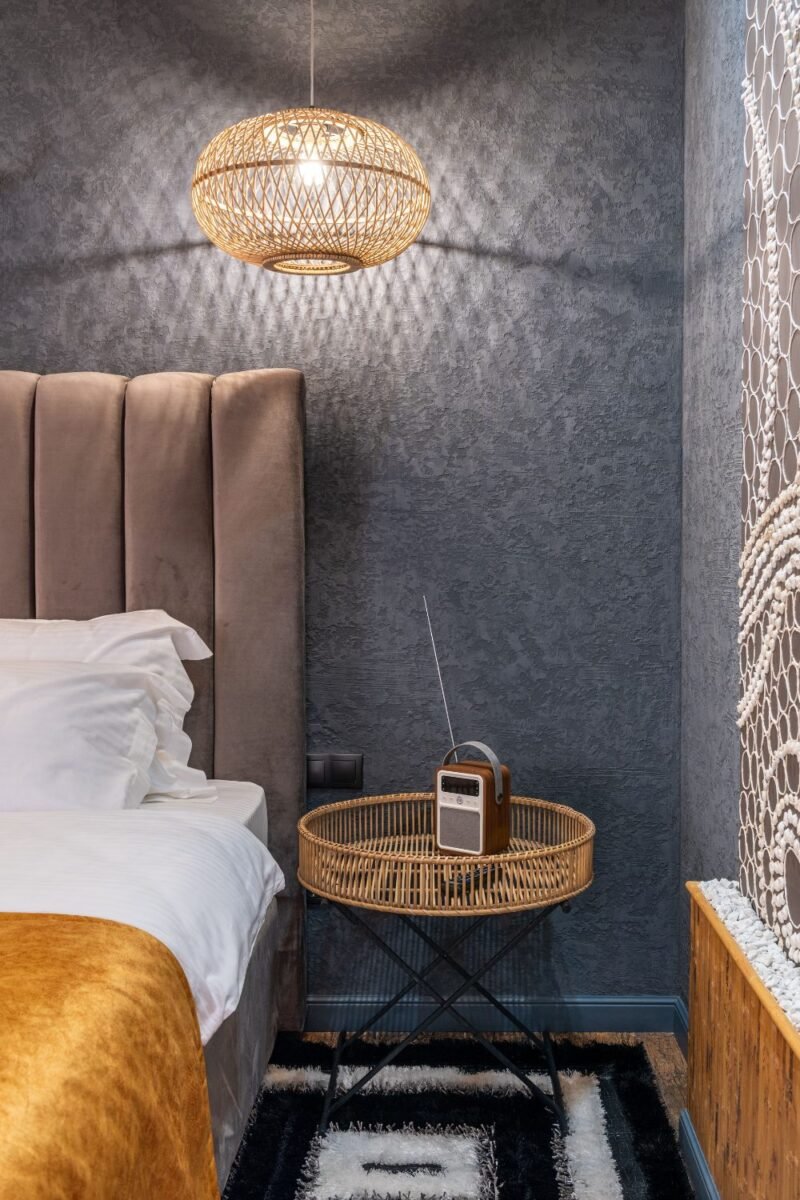 Lit woven pendant light hanging above the bed in a small bedroom, with a padded headboard and a macramé wall hanging