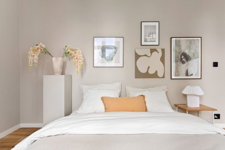 Small bedroom painted in a warm greige with white bedding, framed prints and an ochre accent cushion