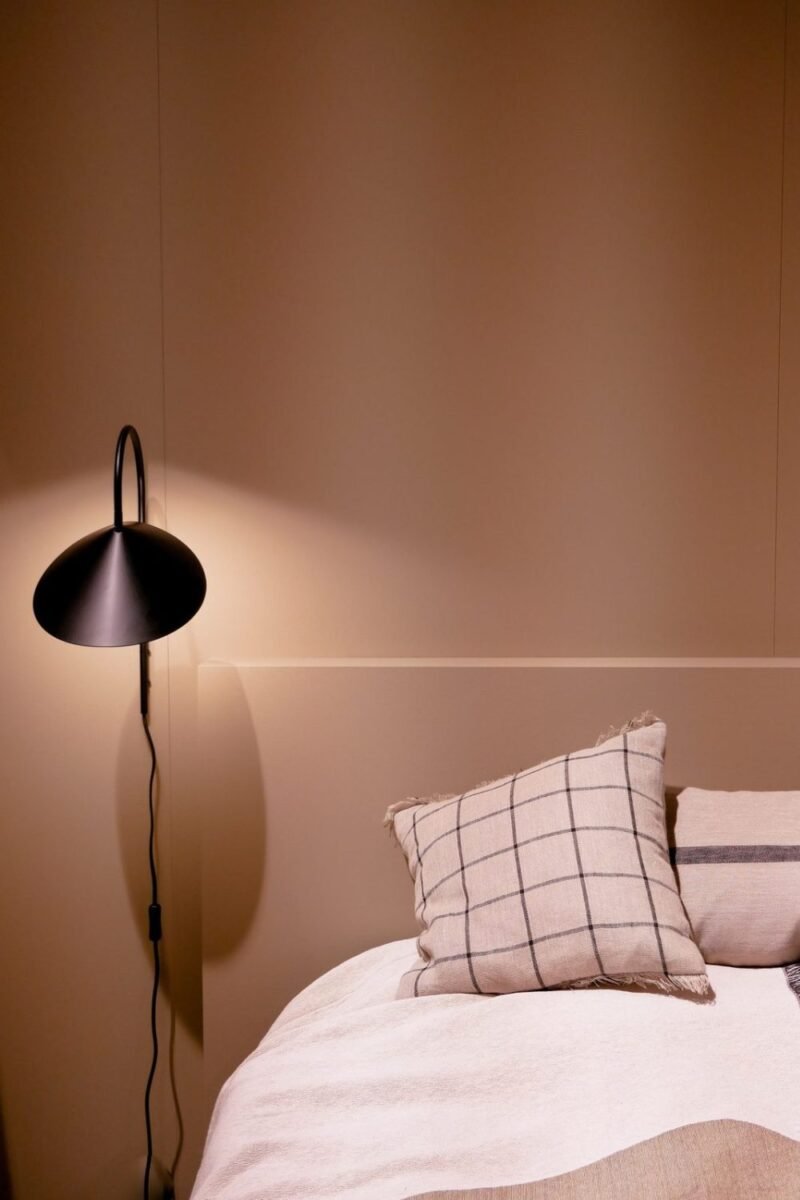 Small bedroom with a warm clay-colored wall, soft pink bedding and a single checked accent pillow