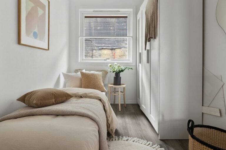 Cozy small bedroom with warm neutral bedding, a plant and framed art, tidy and styled