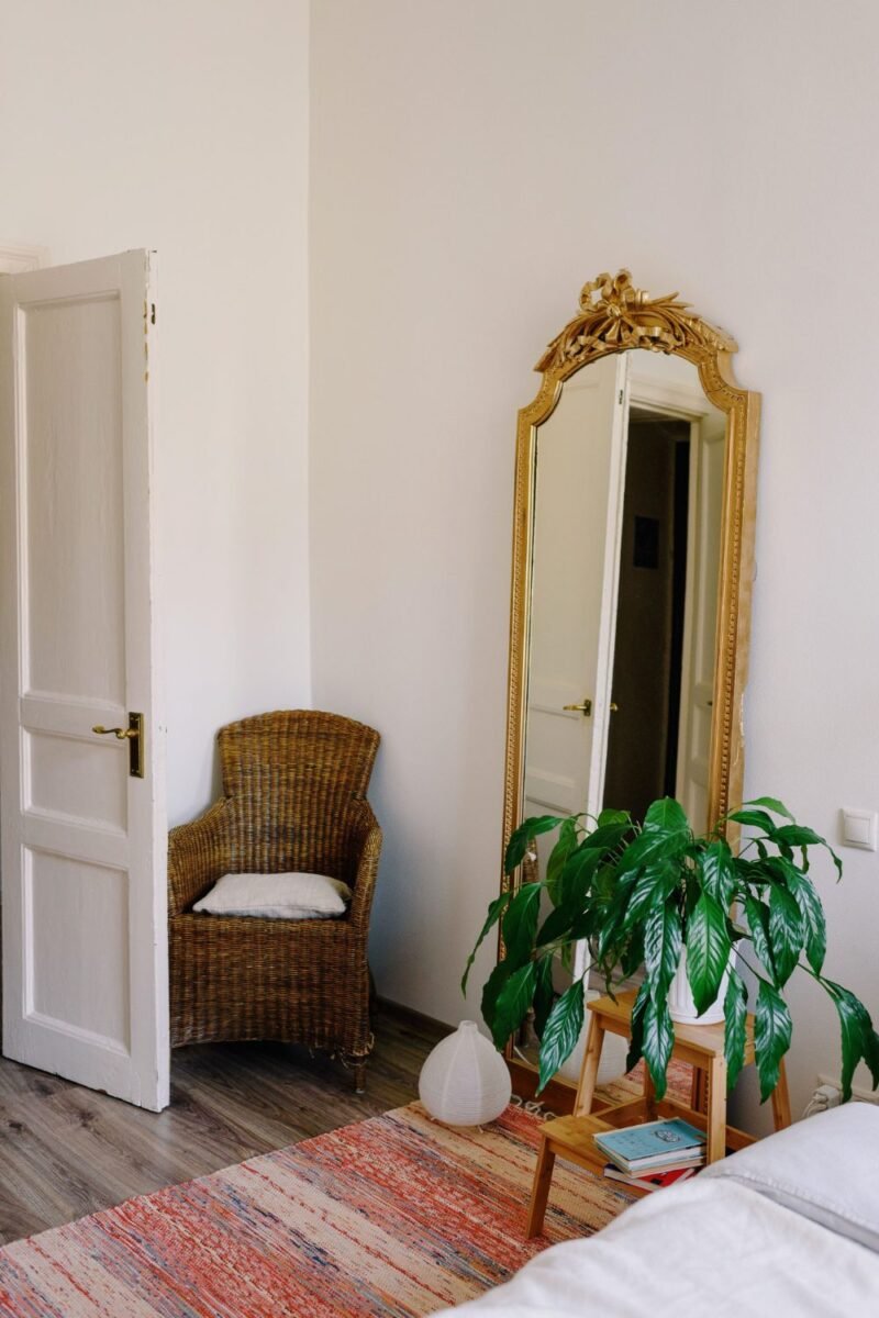 Cozy small bedroom corner with a large leaning mirror, wicker chair and a plant