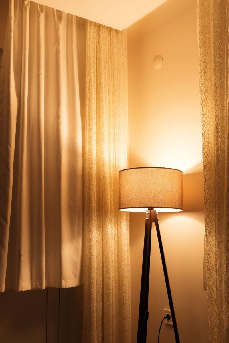 Slim tripod floor lamp glowing warmly in a small bedroom, plugged into the wall with no wiring needed