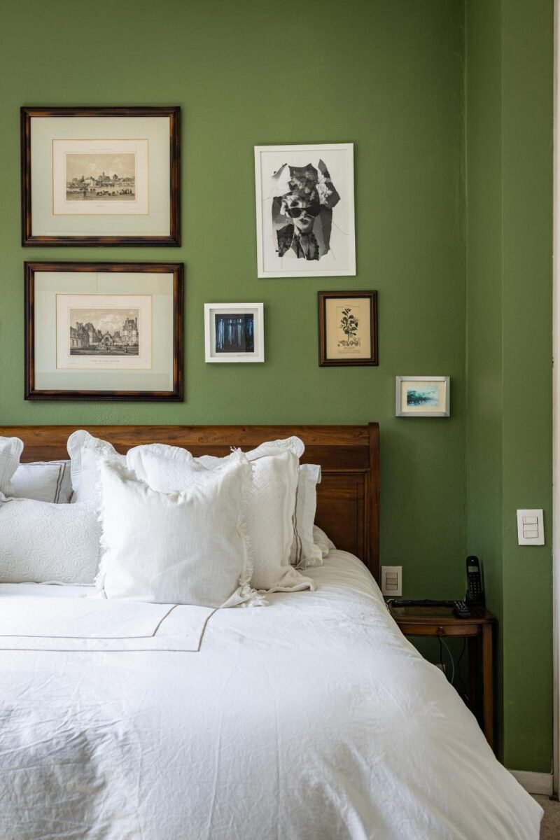 Small bedroom with sage green walls, white bedding and framed prints above a wooden headboard
