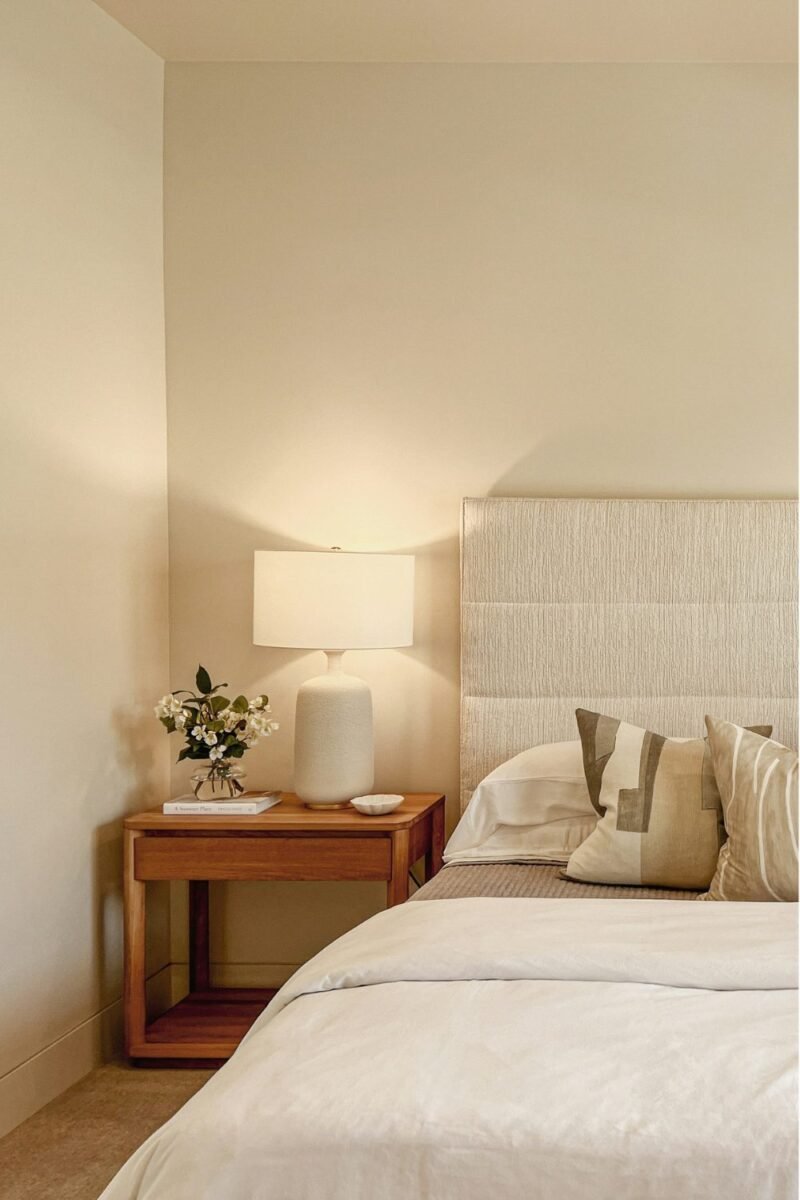Small guest bedroom with a neatly made bed, nightstand, and warm bedside lamp
